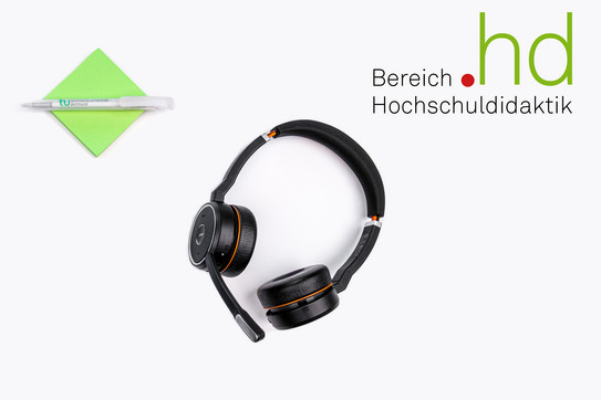 Kopfhörer, links daneben liegt ein Block grüne Klebezettel mit einem TU Dortmund Kugelschreiber darauf, rechts oben steht das Logo des Bereichs Hochschuldidaktik 