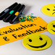 Moderationskarte mit dem Schriftzug "Evaluation & Feeback", gelbe Smilies, Stifte und Moderationsnadeln