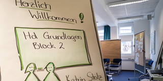 Flipchart mit Begrüßungsposter zum Workshop, im Hintergrund ist der Workshopraum zu sehen