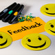 Foto: Moderationskarte mit dem Schriftzug "Feedback", gelbe Smilies, Stifte und Moderationsnadeln