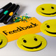 Foto: Moderationskarte mit dem Schriftzug "Feedback", gelbe Smilies, Stifte und Moderationsnadeln