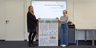 Foto: Joana Eichhorn und Dr. Julia Merger mit einem Projektposter vor einem Bildschirm mit einer Präsentation.
