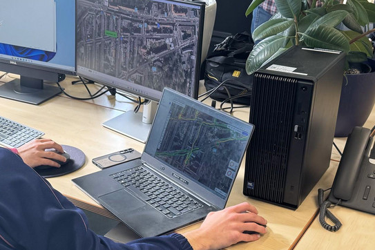 Foto: geöffneter Laptop und ein Monitor auf einem Schreibtisch, die Straßen in einer Satellitenansicht zeigen