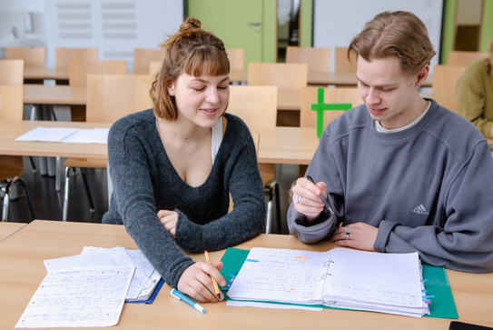 Zwei Studierende im Seminarraum arbeiten zusammen an Unterlagen.