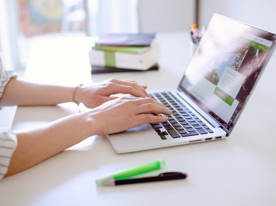 Studentin tippend am Laptop, daneben liegen Bücher und Stifte.