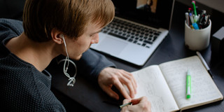 Ein Student arbeitet mit Laptop und Notizbuch.