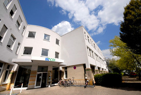 CDI building: The entrance of a white building with two wings from the frog's perspective. In front of it a bicycle stand and right in front of the building trees.
